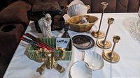 Full view of assorted decor items including lacquered chopsticks, candlesticks, figurines, trays and dishes on a white tablecloth.