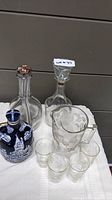 Photo showing all glassware and ceramic decanter on a white cloth, including four etched glasses and three decanters (two glass with stoppers, one ceramic)