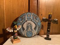 Front view of the two carved totem poles flanking the large painted drum showing Native American imagery.