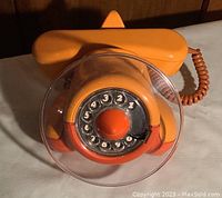 Front view of orange airplane rotary telephone with clear dial guard