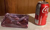 Purple glass ashtray placed next to a soda can for size reference, displays geometric faceted design.