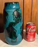 Front view of vase next to a Coke can to show scale and colors of turquoise blue with dark green and black splotches.