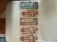 Photo showing one blue $5 Canadian dollar bill with signs of heavy use and four brown $2 Canadian bills, all featuring Queen Elizabeth II.