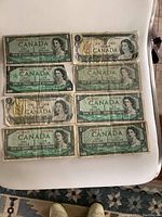 Front side view of eight Canadian one dollar bills arranged in two columns, showing Queen Elizabeth II portrait and denomination.