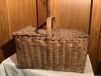 Front and side view showing rectangular shape, woven construction, and hinged lids with handle.