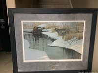 Framed print showing winter river scene with two wolves, snow, and bare brush.