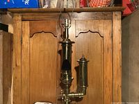 Front view of tall brass steam whistle lamp showing detailed vertical brass cylinder with side chamber against wooden background.
