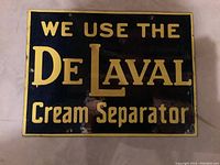 Front view of sign showcasing navy blue enamel and yellow text: “WE USE THE De LAVAL Cream Separator.”