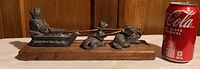 Side view of soapstone sculpture on wooden base, showing the figure in the sled and four dogs pulling it, with a soda can for size reference.