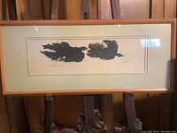 Framed woodblock print 'Birds in Flight' by Ken Tunneli, displayed on an easel against a wooden wall. The print shows black bird silhouettes in flight on light background, with signature and edition number visible.