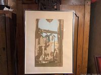 Framed woodblock print of abstract window reflection in earth tones with light blue, displayed upright against wooden backdrop.