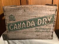 Front view of wooden crate showing Canada Dry logo and text on weathered wood surface.