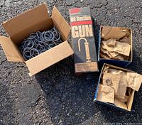 Two cardboard boxes with numerous galvanized metal ring bushings with threaded screw ends. Next to them is a tall box labeled RP Oil Suction Gun and two smaller boxes partially open containing metal bushings wrapped in paper.