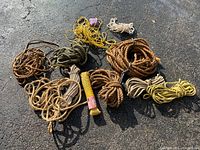 Overview of assorted ropes in different sizes, colors, and materials loosely arranged on asphalt surface.