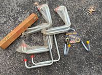 Five assorted metal tool hangers arranged on the ground including L-shaped, U-shaped, and one capped with yellow labeled 'Hang All'.