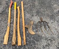 Top down view of four wooden tool handles and two rusted metal tool heads on asphalt.