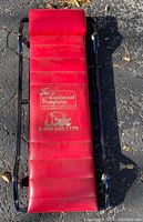 Top view of red padded creeper showing The Eastwood Company branding and phone number on vinyl surface with stitching detail.