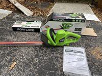 Full view of the Portland 22-inch electric hedge trimmer with original box and owner's manual on pavement.