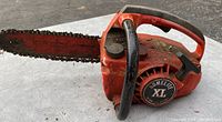 Side view of Homelite Lil Red XL UT 10507-4 chainsaw showing red body, black handle, saw chain with signs of wear.