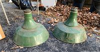 Two large vintage green metal industrial lights shown from side angle outdoors on asphalt with dried leaves scattered around.