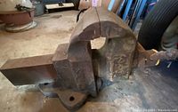 Side view of the large iron vise showing its curved and solid cast metal body with a screw handle.