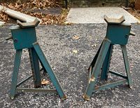 Pair of blue metal jack stands placed on paved ground showing overall view and condition.