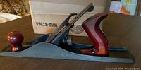 Side view of vintage steel hand planer showing wooden handles and metal body.