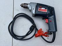 Full view of the Skil 3/8 inch electric drill showing the body, chuck, trigger, and attached power cord with clamps.
