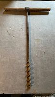 Complete view of the vintage auger showing the wooden T-handle and metal spiral bit on a neutral background.