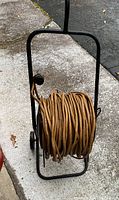 Side view of black metal hose reel frame with coiled brown wire or hose around the reel.