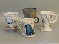 Four abstract ceramic coffee cups arranged together, showing all designs and shapes distinctly.