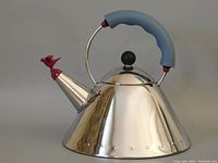 Side view of kettle showing conical stainless steel body, curved blue handle and red whistle.