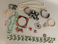 Top down view of entire lot spread on table showing varied jewelry items including pearl necklace, multi-beaded necklace, bangles, brooches, earrings, and pendants.