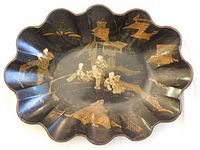 Top view of black scalloped-edge papier-mache bowl with gold and cream painted Chinoiserie scene including figures and architectural motifs.