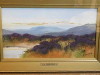 Close-up of painting showing landscape, mountains, purple shrubs and artist signature