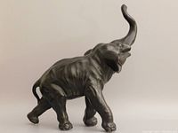 Side profile of the large bronzed elephant sculpture showing detailed texture and pose with raised trunk.