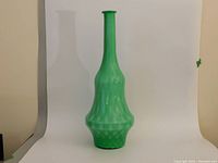 Tall green Murano glass vase with quilted pattern on a plain backdrop.