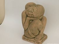 Front and angled views of the stone sculpture showing the seated woman with head resting on her hands and legs drawn up.