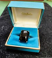 Oblong black onyx solitaire ring displayed inside a teal Gimbels box lined with turquoise velvet.