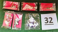 Five packages of earrings with various designs including Snoopy, panda, and charms shown on green surface with lot number card