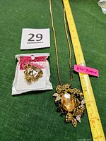 Photo showing the necklace and pin laid flat with ruler for size reference. Necklace has a large oval amber gem surrounded by gold filigree leaves and rhinestones. The pin is gold-tone bee with amber and clear stones in original packaging.