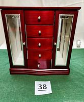 Front view of cherry wood jewelry box with five drawers and two mirrored doors closed.