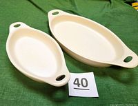 Two beige oval Corning Ware stoneware dishes with handles placed on a green cloth, showing overall shape and size comparison.