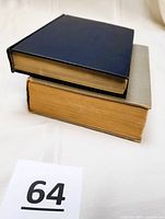 Two hardcover books stacked, showing the top and side edges with yellowing pages, one with blue cover and one with gray cover.