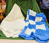 Two afghans displayed side by side: one entirely white with intricate crocheted patterns, the other made from blue and white crocheted squares.