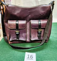 Front view of plum-colored leather hobo bag with two front buckle pockets and adjustable shoulder strap.