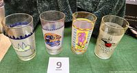 Four tall glasses arranged side by side featuring colorful racing-themed logos and text related to Kentucky Derby and Belmont Stakes.
