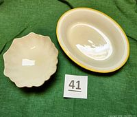 Top-down view of two Lenox dishes on green cloth, showing oval cream colored dish with gold rim and smaller scalloped footed dish