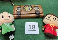 Dark brown wristlet with Hogwarts crest on front, placed between two small plush characters dressed in Harry Potter-themed robes, photo of full lot items
