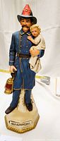 Front view of the 15-inch ceramic firefighter decanter holding a baby and lantern.